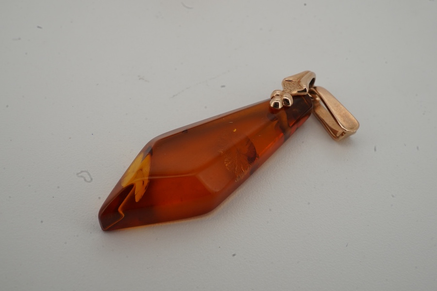 A yellow metal and enamel globe charm, reading 'The whole world turns round the love', height 3.2cm; and a gold and amber pendant, length 4.5cm, Russian assay marks for 14ct gold